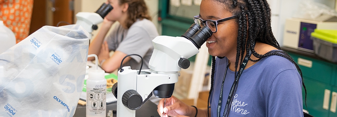 A student looking into a microscope in a biology lab.