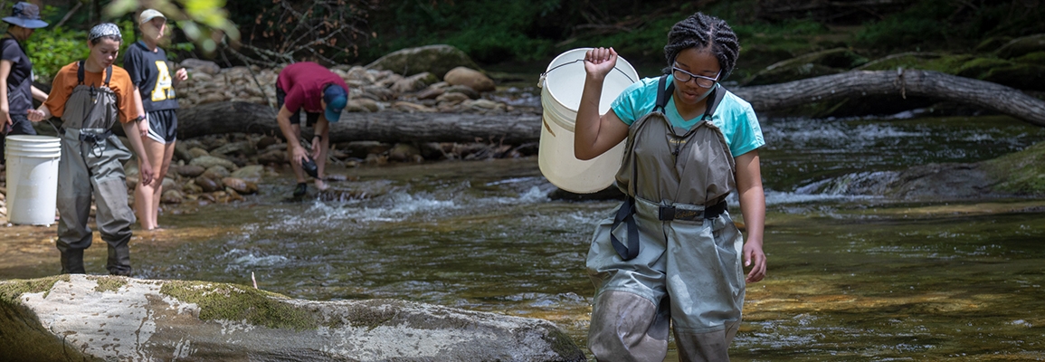 A student conducting water sampling in a river.